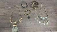 Photo showing assortment of jewelry on wooden floor including necklaces, choker, arm band, bracelet, and pendant.