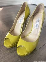 Front view of yellow patent leather Jimmy Choo peep toe heels showing interior label and toe design.