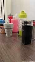 Photo showing a variety of bottles including collapsible cup, protein shaker, and water bottles on floor.
