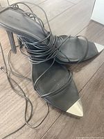 Close-up photo of one black stiletto heel shoe with silver pointed toe cap and multiple thin black lace-up straps.