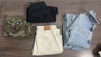 Four pairs of pants laid out on the floor including a light blue Levi's denim jumper, black pants, camouflage cargo pants, and cream Levi's jeans.