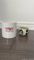 Photo of two planters on floor, white planter with text and smaller round floral planter