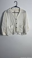 Front view of a light cream or off-white women's button-up top on a black hanger against a white wall.