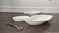 Three white ceramic medium serving bowls in leaf and oval shapes and one metal bottle opener on floor.