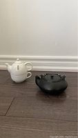 Photo of two teapots side by side showing the white ceramic tea-for-one pot and the black cast iron teapot.