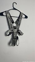 White harness with printed black 'UNTITLED & CO' branding on straps hanging on black hanger against white wall.