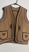 Front view of a brown vintage wool vest with dark brown trim, front pockets, and geometric embroidery on pockets and front sides.