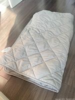 Folded light gray weighted blanket displayed on wooden floor, showing quilted square pattern and fabric texture.