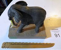 Elephant bookend with detailed textured carving, long tusks, mounted on base with 'KAMBAKU' label, alongside wooden carved elephant letter opener with decorative cutouts.