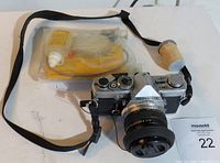 Olympus OM-1 film camera with attached lens, camera strap, film canister, and a cleaning kit in the background.