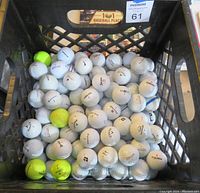 Partial crate filled with approximately 70 used golf balls in a black crate, primarily white balls with a few yellow ones.