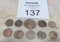 Top view of 10 ancient Roman bronze coins arranged in two rows, showing varied wear, cleaning effects, and sizes on marble surface under auction lot number 137