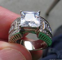 Close-up front view of the silver-toned ring showing the large square-cut clear man-made gem center piece and multiple smaller gems on the band.