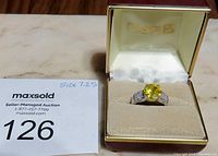 Ring displayed inside its red and cream jewelry box with 'FIEGES' name, showing the bright yellow citron gemstone and accent stones on band.