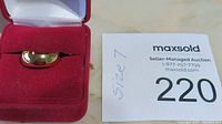 Gold wedding band displayed in red jewelry box with auction label showing size and lot number.