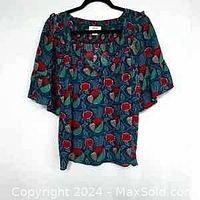 Front view of Anthropologie Mave shirt with floral pattern on green background hung on hanger.