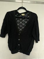 Front view of the black Aritzia Wilfred short sleeve cardigan showing button closure and subtle diamond pattern.