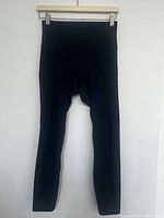 Front view of the navy blue yoga pants hanging on a wooden hanger against a white wall.