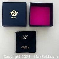 Top view of black square jewelry box with gold Jet Set Candy logo on lid and pink interior lining.