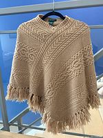 Front view of brown knitted poncho showing cable knit pattern and fringed hem.