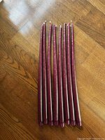 Eight tall burgundy taper candles displayed upright on a wooden surface.