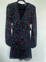Full front view of the Kooples dress showing navy blue fabric with red rose and leaf pattern, fitted waist with peplum, long sleeves, and pleated skirt.