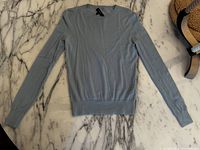 Full view of the baby blue long sleeve Theory sweater laid flat on marble surface showing the front with ribbed neckline, cuffs and waistband.