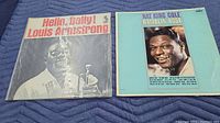 Front cover of two vintage vinyl albums, 'Hello, Dolly!' by Louis Armstrong and 'Ramblin' Rose' by Nat King Cole, shown folded with clear visible titles and artist names.