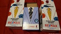 Three boxes of bobblehead figurines with Remax and Kidney Foundation branding promoting organ donation, showing suit and tie prints.