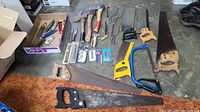 Various hand saws, hammers, wire cutters, and cutting tools arranged on the floor