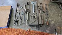 View of assorted specialty tools, including pliers, tongs, chain tool, and pullers laid out on a concrete floor.
