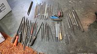 Overview of various vintage metal files and rasps laid out on floor with diverse handle types.