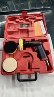 Open red carrying case containing Astro air polishing tool and two polishing pads, one black and one cream colored on foam bases.