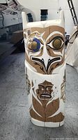 Front view of carved cedar totem pole depicting owl face and smaller figure below