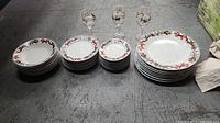 Photo of stacks of dinnerware and glasses arranged in a row: dinner plates, salad plates, smaller plates and decorative wine glasses, large serving platters