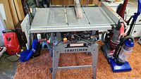 Front angled view of the Craftsman 10-inch table saw showing the metal tabletop, blade, stand, and surrounding garage items.
