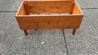 Rectangular wooden garden box with solid plank sides and four short legs, viewed from a low angle showing front and side.