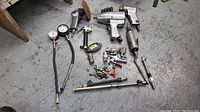 Lot overview showing various pneumatic air tools, tire pressure gauges with hoses, sockets, and fittings on concrete floor.