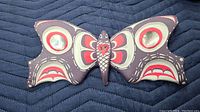 Front of wooden butterfly showing painted indigenous design and inset shell pieces