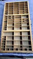 Front view of the wooden letter press block tray showing rectangular compartments of various sizes under natural light on a blue blanket.