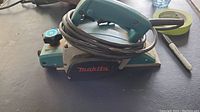 Side view of Makita electric planer showing Makita logo, handle, power cord, and adjustment knob.