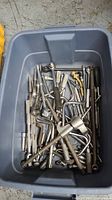 Top view of gray plastic bin filled with assorted metal ratchets, extensions, and hand tools.