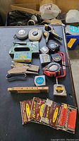 Photos displaying miscellaneous staplers, tape measures, clamps, and measuring tools arranged on a black surface.