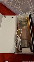 Clear cylindrical water generator bottle with silver top and base, placed inside white box along with a USB charging cable.