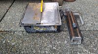 Full view of Q.E.P tile saw with yellow blade guard and rusted metal cutting table alongside a metal tile cutter with rusted rails and cutting wheel