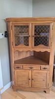 Front view of solid maple corner hutch unit with closed glass-paned upper doors and closed lower cabinet doors.