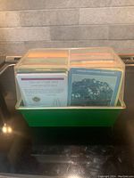 Top view of vintage plant collector cards stored in a green plastic box with visible dividers showing card titles such as African Violets and Germanders, and Houseplants.