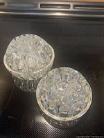 Clear top-down view of two vintage glass flower frogs showing multiple rounded opening holes. The one on the left is larger, approximately 4 inches in diameter, while the smaller one is about 3 inches.