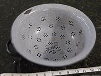 Top view showing the white speckled interior with floral pattern perforations of the antique graniteware strainer and two handles.