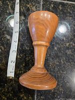 Overall front view of antique wooden goblet placed on a dark granite counter next to a measuring tape showing approx. 5.5 inches height.